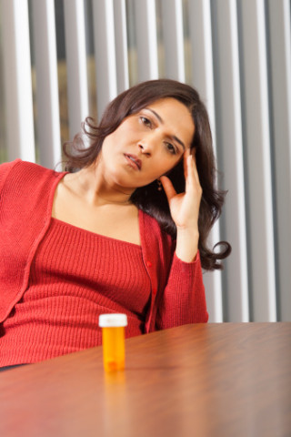 Businesswoman contemplating medicine at desk