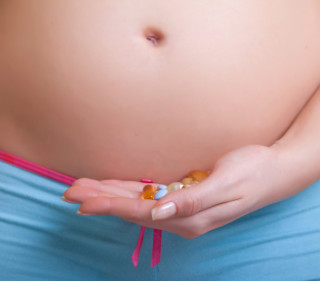 Pregnant woman holding prescription drugs near belly on neutral