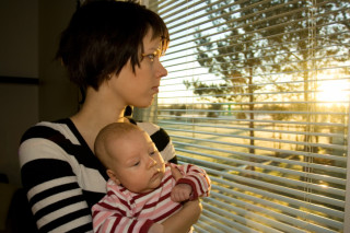 Young mother looking out from the window with her baby 2